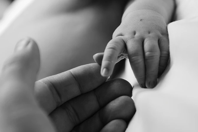 A premature infant's feet supported by a gloved hand during phototherapy in the NICU